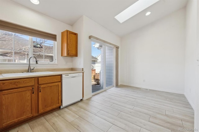 kitchen with lofted ceiling with skylight, sink, white dishwasher, and light hardwood / wood-style floors