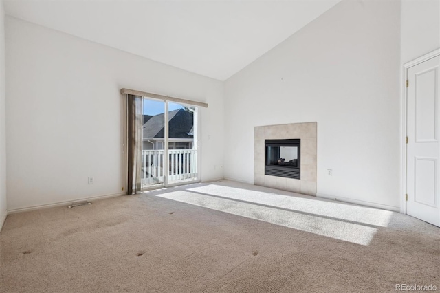 unfurnished living room featuring a tile fireplace, carpet floors, and high vaulted ceiling