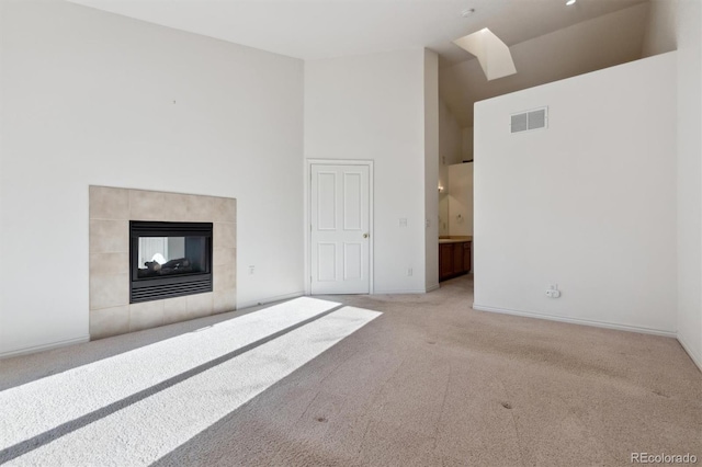 unfurnished living room featuring light colored carpet, a high ceiling, and a tiled fireplace