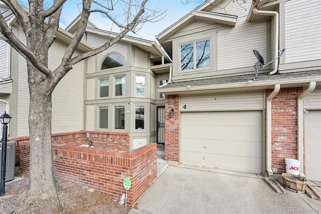 townhome / multi-family property featuring brick siding, a shingled roof, central AC unit, a garage, and driveway