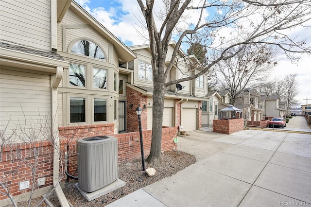 view of home's exterior featuring central AC, brick siding, driveway, and an attached garage