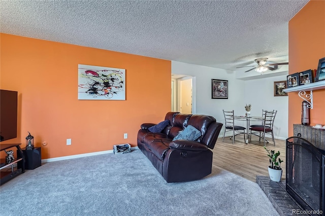 living room with ceiling fan, carpet, a fireplace, and a textured ceiling