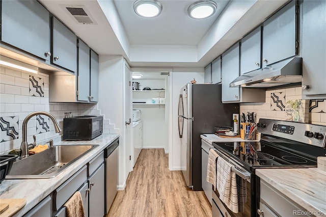 kitchen with appliances with stainless steel finishes, tasteful backsplash, light hardwood / wood-style floors, sink, and a raised ceiling