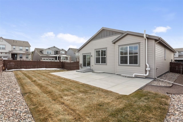 back of property with entry steps, a patio, a fenced backyard, a yard, and board and batten siding