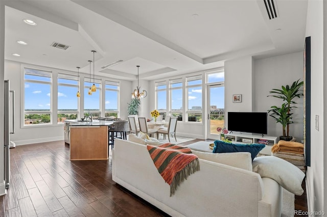 living room featuring dark hardwood / wood-style floors, plenty of natural light, a tray ceiling, and a notable chandelier