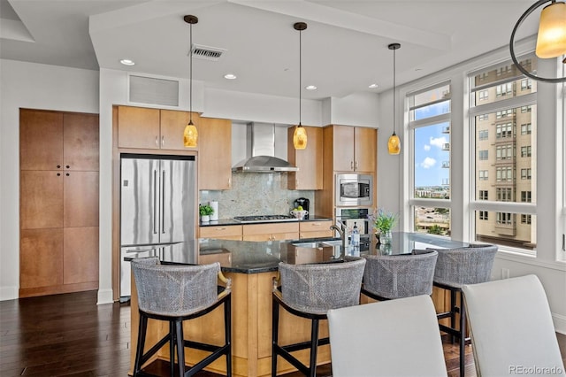 kitchen with wall chimney exhaust hood, dark wood-type flooring, hanging light fixtures, stainless steel appliances, and decorative backsplash