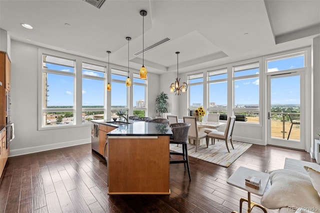 dining area with an inviting chandelier, a raised ceiling, a wealth of natural light, and dark hardwood / wood-style floors