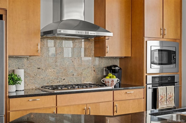 kitchen featuring dark stone countertops, appliances with stainless steel finishes, wall chimney range hood, and decorative backsplash