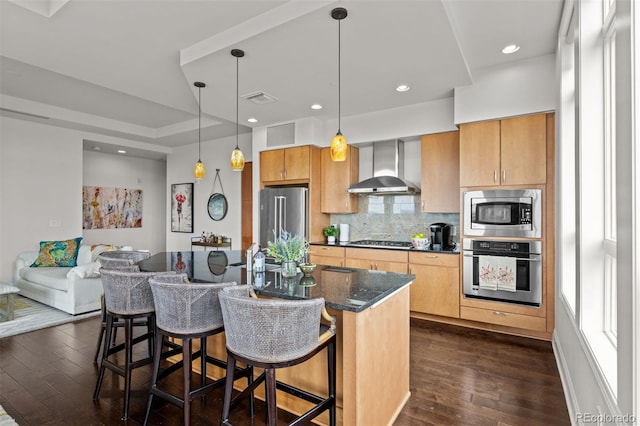 kitchen featuring pendant lighting, wall chimney range hood, dark wood-type flooring, stainless steel appliances, and a kitchen breakfast bar