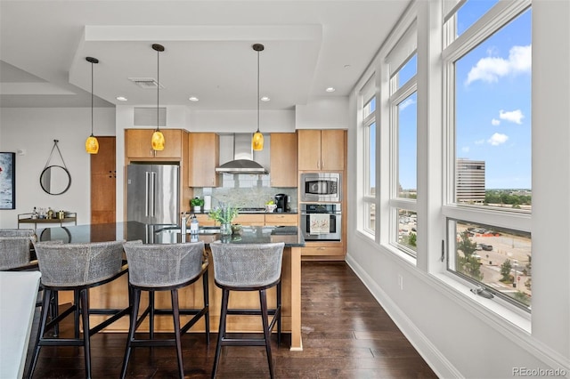 kitchen featuring appliances with stainless steel finishes, pendant lighting, wall chimney range hood, and a kitchen breakfast bar