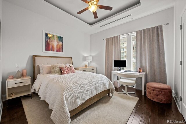 bedroom featuring dark hardwood / wood-style floors, ceiling fan, and a tray ceiling