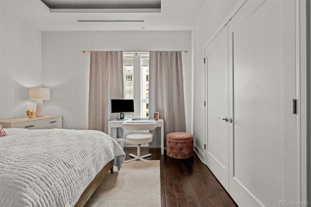 bedroom featuring a closet, dark hardwood / wood-style floors, and a raised ceiling