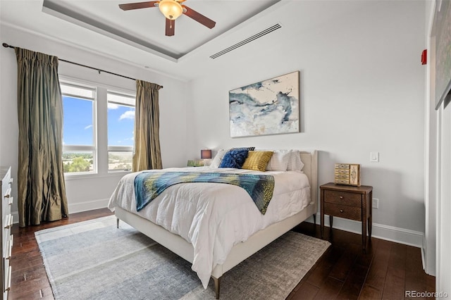 bedroom with dark hardwood / wood-style floors, a raised ceiling, and ceiling fan