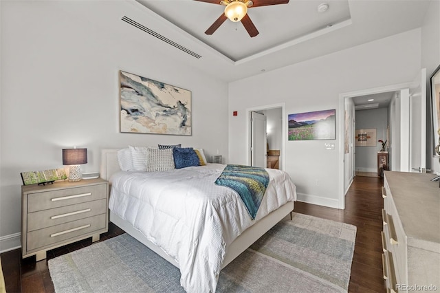 bedroom with a raised ceiling, dark hardwood / wood-style floors, ceiling fan, and ensuite bath