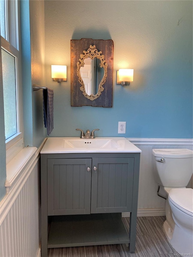 half bathroom featuring toilet, a wainscoted wall, vanity, and tile patterned floors