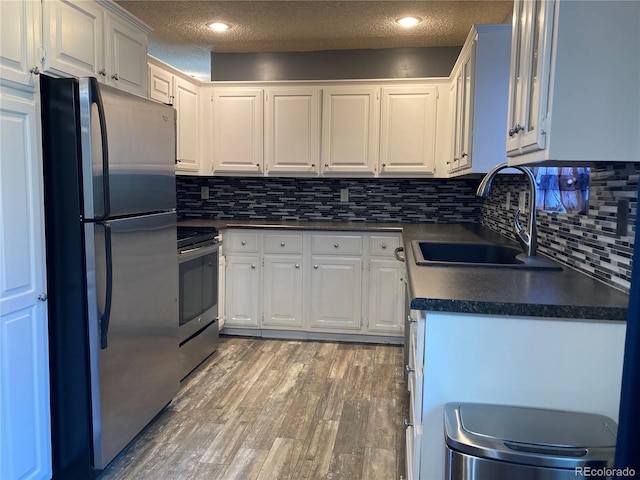 kitchen featuring stainless steel appliances, a sink, dark countertops, light wood finished floors, and white cabinets