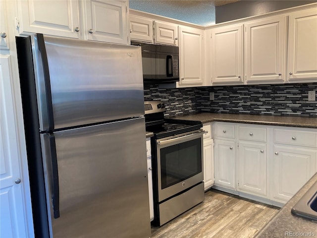 kitchen featuring appliances with stainless steel finishes, dark countertops, light wood finished floors, and white cabinets