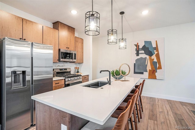 kitchen featuring hanging light fixtures, light wood-type flooring, appliances with stainless steel finishes, backsplash, and sink