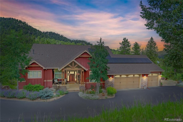 31189 Manitoba Dr, Evergreen, CO 80439 - view of front of house featuring a garage, solar panels, stone siding, asphalt driveway, and roof with shingles