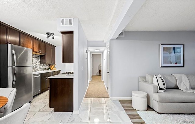 kitchen featuring open floor plan, appliances with stainless steel finishes, dark brown cabinets, light countertops, and baseboards