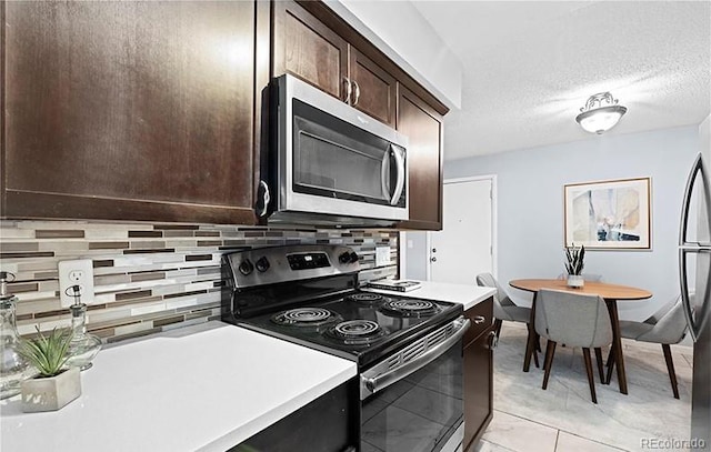 kitchen with appliances with stainless steel finishes, decorative backsplash, dark brown cabinetry, light countertops, and a textured ceiling