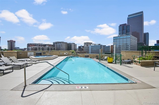 community pool featuring a patio, a hot tub, and a city view