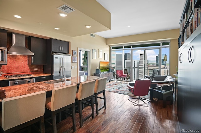 kitchen with visible vents, wall chimney exhaust hood, open floor plan, stainless steel appliances, and a sink