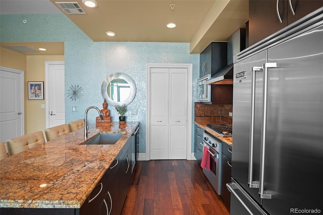 kitchen featuring built in appliances, a sink, visible vents, light stone countertops, and wall chimney exhaust hood