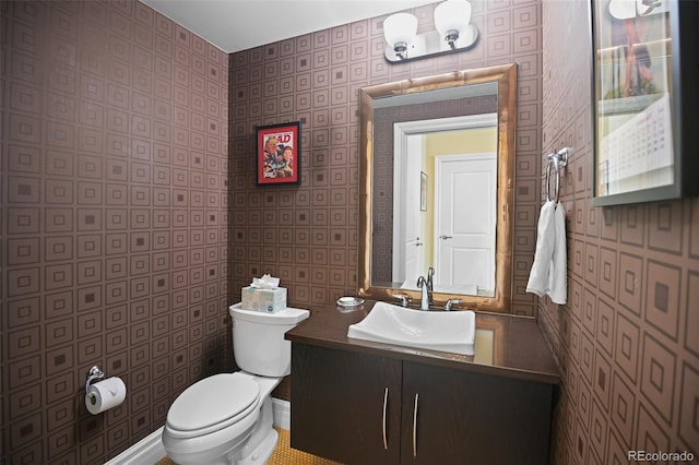 half bathroom with toilet, wallpapered walls, and vanity