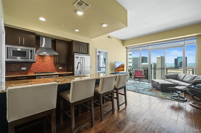 2001 Lincoln St Unit 2420, Denver, CO 80202 - kitchen featuring wall chimney exhaust hood, stainless steel appliances, a breakfast bar, tasteful backsplash, and dark wood-type flooring