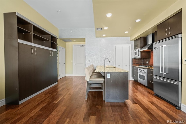 2001 Lincoln St Unit 2420, Denver, CO 80202 - kitchen with built in appliances, a sink, wall chimney range hood, dark wood-type flooring, and a breakfast bar area