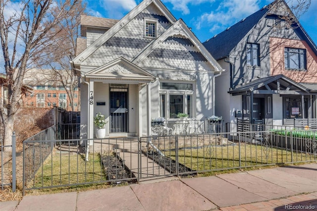 victorian-style house featuring a fenced front yard, covered porch, a shingled roof, and a front lawn