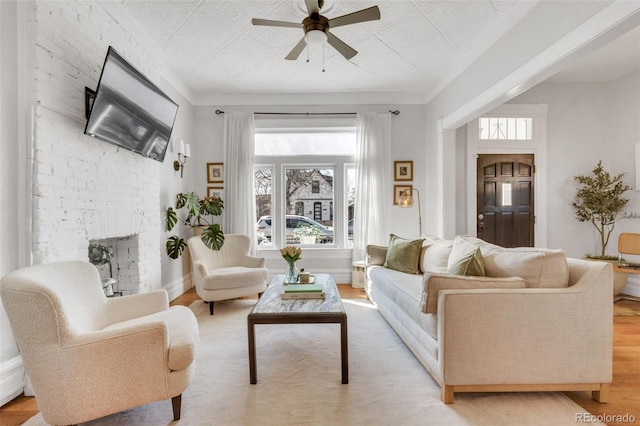 living room featuring ceiling fan, light wood-type flooring, a fireplace, and an ornate ceiling