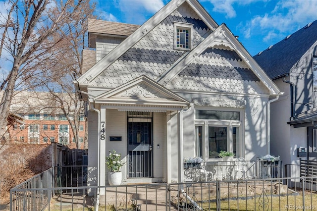 victorian house featuring a fenced front yard, covered porch, and a shingled roof