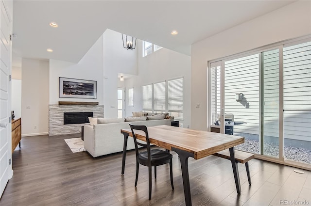 dining area with a high ceiling, wood-type flooring, and a stone fireplace