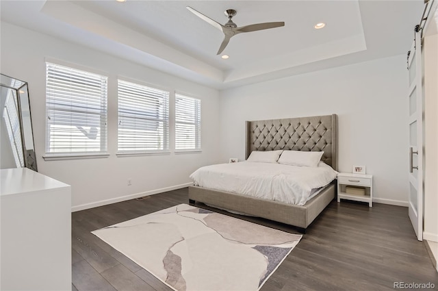 bedroom featuring a tray ceiling, multiple windows, ceiling fan, and dark hardwood / wood-style flooring