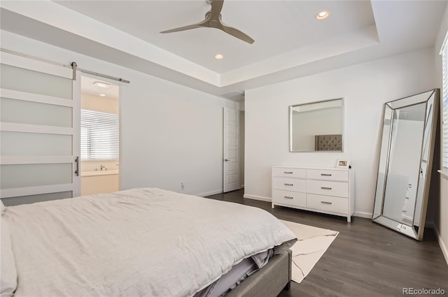 bedroom featuring a barn door, a raised ceiling, ceiling fan, ensuite bathroom, and dark hardwood / wood-style floors