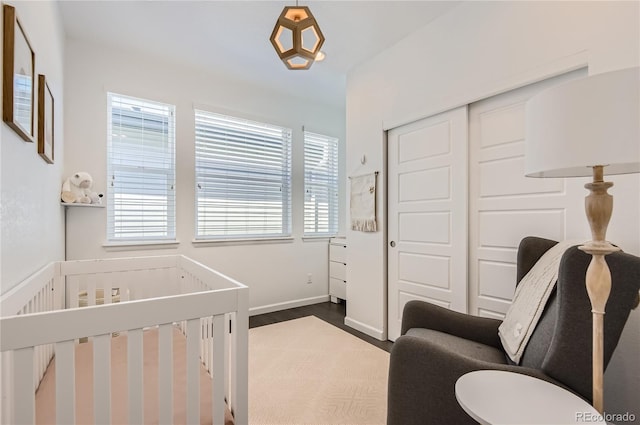 bedroom with a crib, dark hardwood / wood-style flooring, and a closet