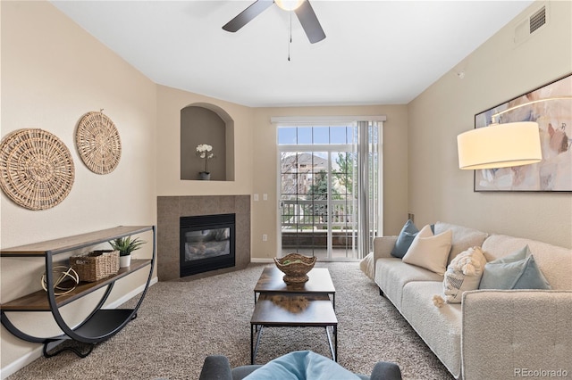 carpeted living room with a ceiling fan, a tile fireplace, visible vents, and baseboards