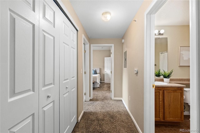 corridor featuring baseboards, dark carpet, and a sink
