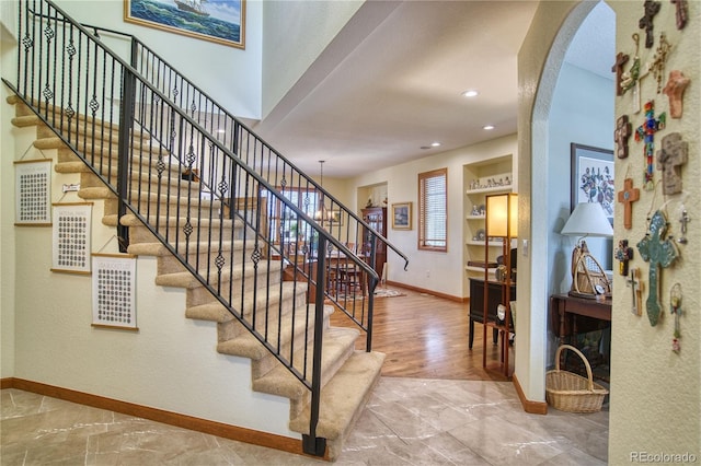 staircase with arched walkways, baseboards, and recessed lighting