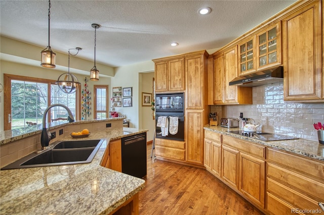 kitchen featuring light wood finished floors, under cabinet range hood, a sink, black appliances, and a textured ceiling