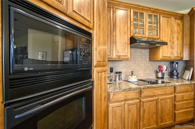 kitchen featuring backsplash, under cabinet range hood, brown cabinets, and glass insert cabinets