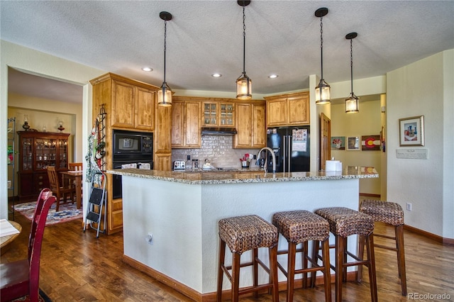 kitchen with brown cabinetry, dark wood finished floors, black appliances, and tasteful backsplash
