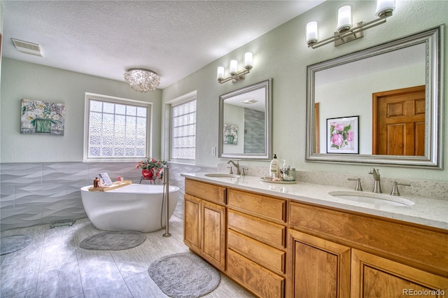 bathroom with a freestanding tub, visible vents, a sink, and a textured ceiling