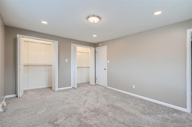 unfurnished bedroom featuring two closets and light colored carpet