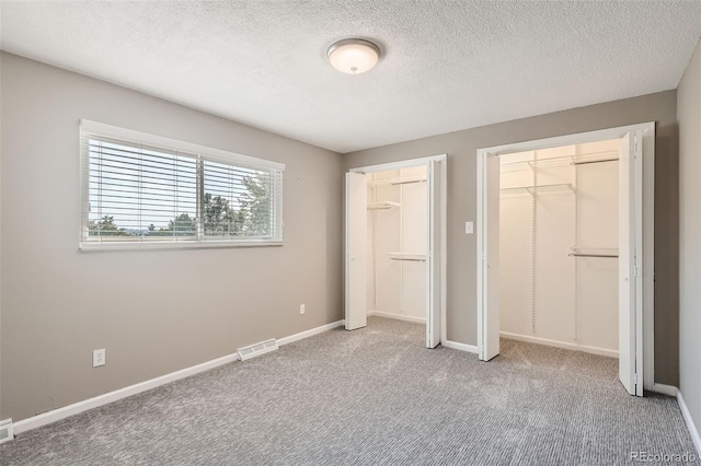 unfurnished bedroom with two closets, a textured ceiling, and carpet