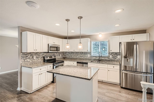 kitchen featuring sink, a center island, hanging light fixtures, stainless steel appliances, and white cabinets