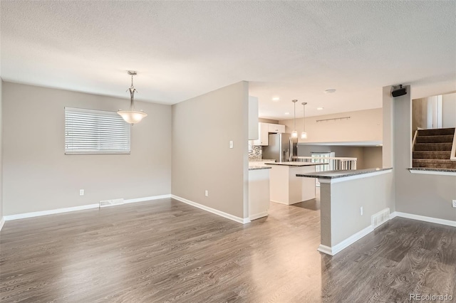 kitchen with dark wood-type flooring, stainless steel refrigerator with ice dispenser, kitchen peninsula, pendant lighting, and white cabinets