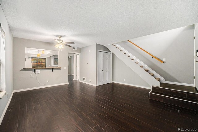 unfurnished living room with stairway, ceiling fan, wood finished floors, baseboards, and a textured ceiling